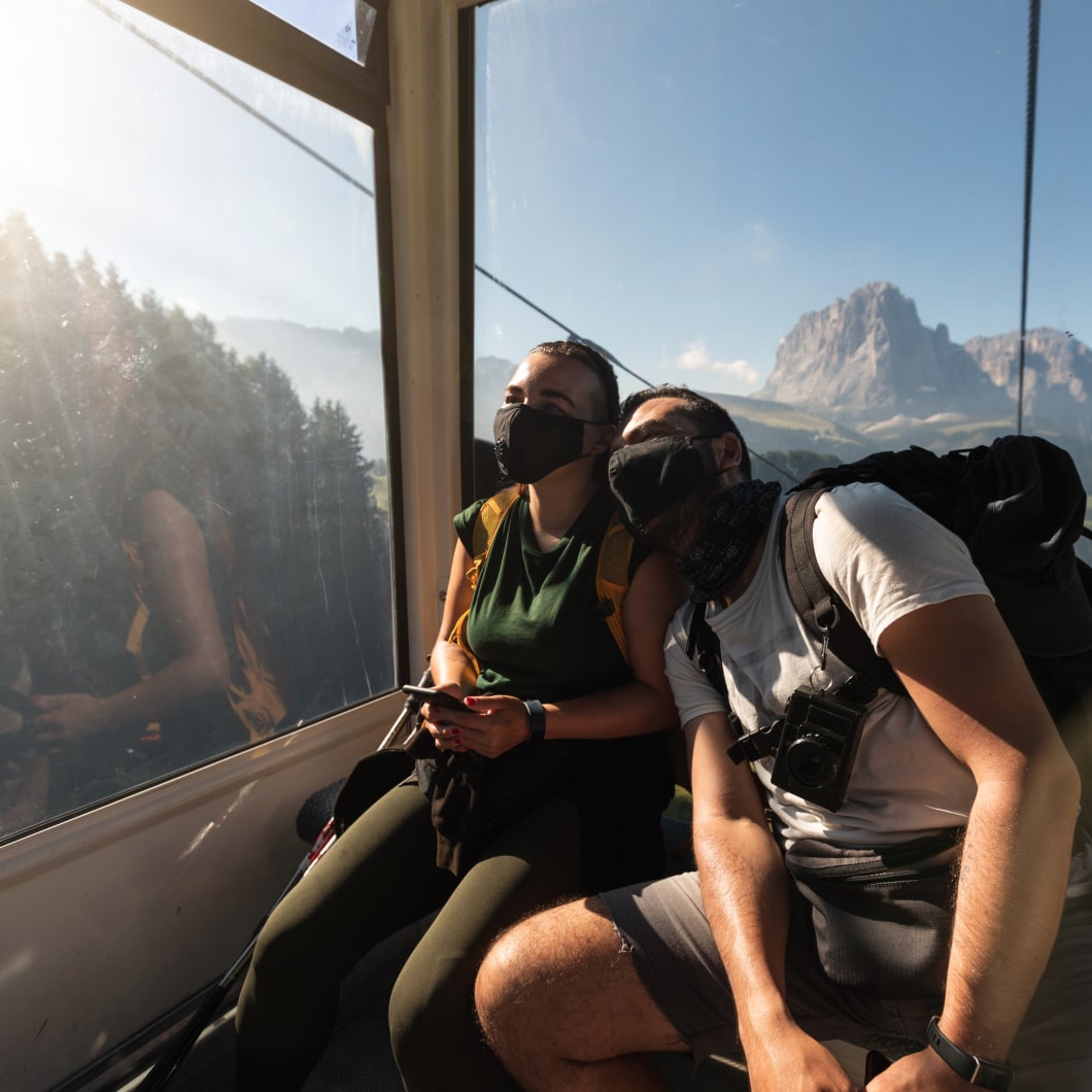 Couple wearing masks riding a gondola through a mountain range