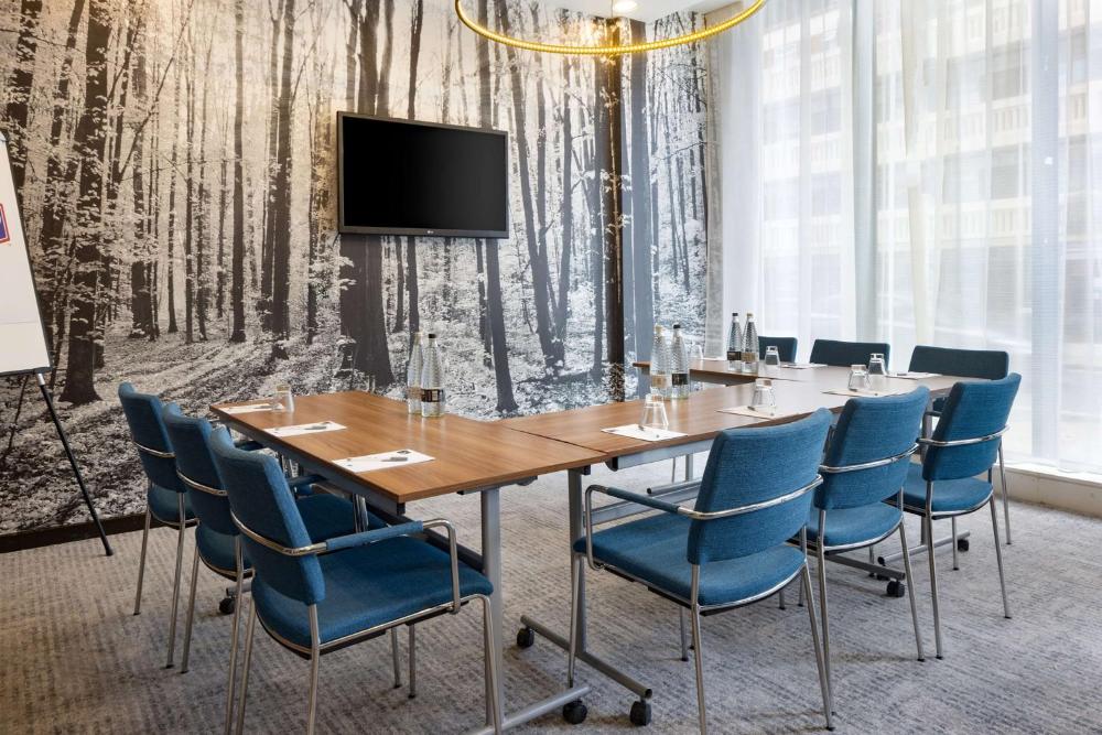 Meeting room with a wooden conference table, blue chairs, and screen at Hampton by Hilton London Waterloo