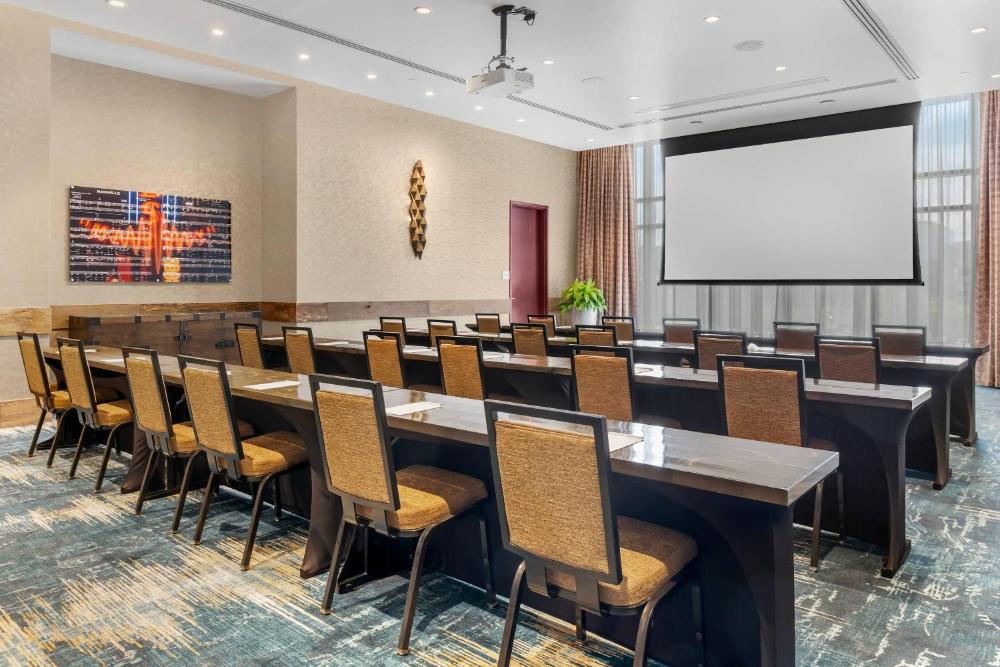 Conference room with rows of tables, chairs, and a projection screen at Cambria Hotel Nashville Downtown