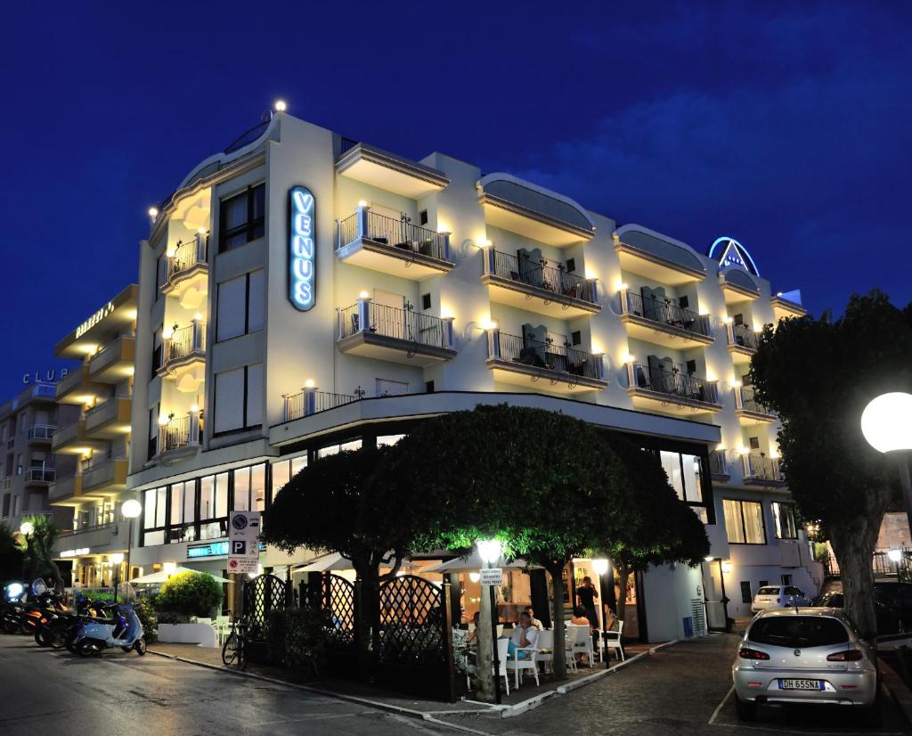 - un grand bâtiment blanc avec un panneau la nuit dans l'établissement Hotel Venus, à Gabicce Mare