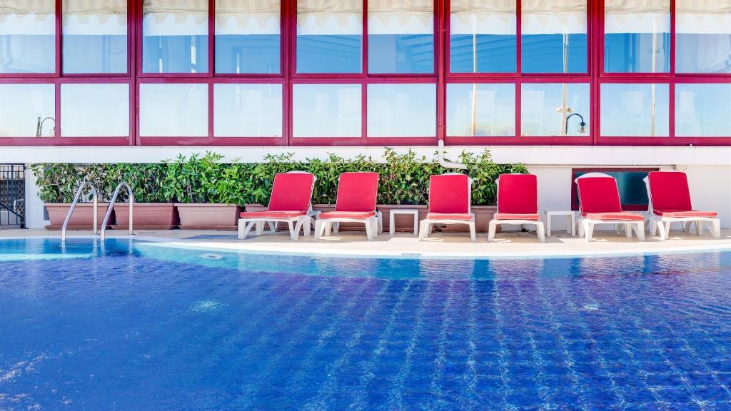 une rangée de chaises rouges à côté d'une piscine dans l'établissement Hotel Manila, à Lido di Jesolo