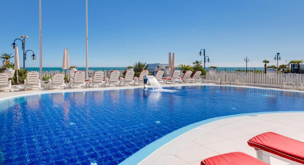 une grande piscine avec des chaises et une fontaine dans l'établissement Hotel Manila, à Lido di Jesolo