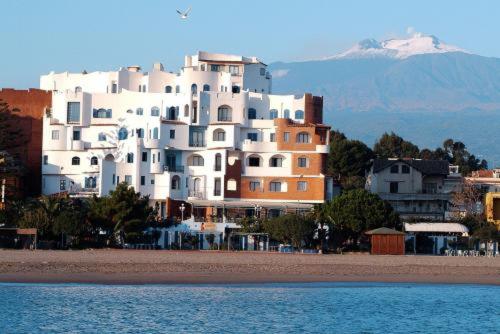 - un grand bâtiment blanc au sommet d'une plage dans l'établissement Sporting Baia Hotel, à Giardini Naxos
