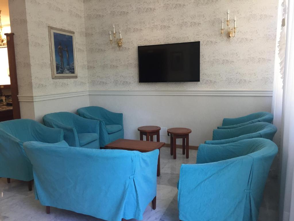 une salle d'attente avec des chaises bleues et une télévision à écran plat dans l'établissement Hotel Consuelo, à Lignano Sabbiadoro