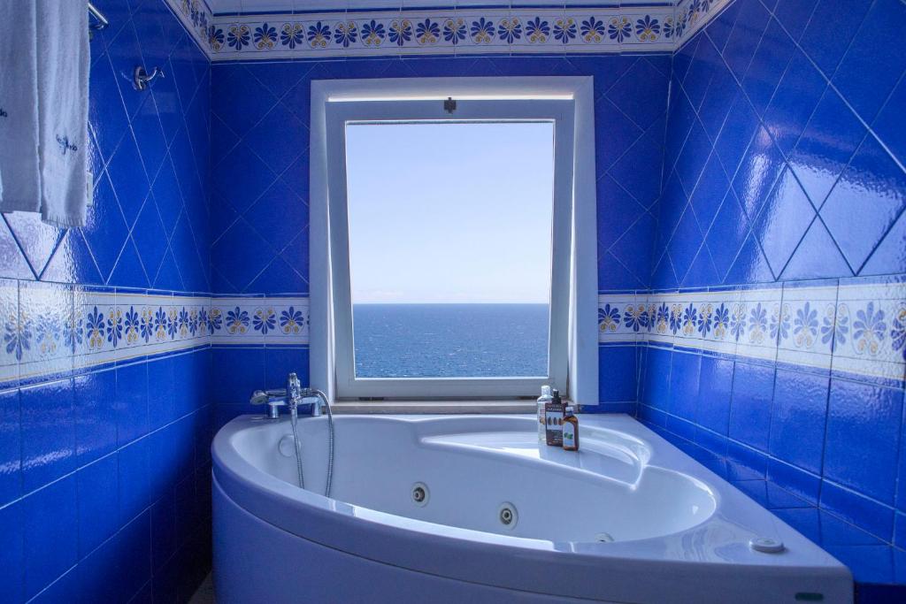 une salle de bain bleue avec une baignoire et une fenêtre dans l'établissement Hotel Piccolo Mondo, à Castro di Lecce