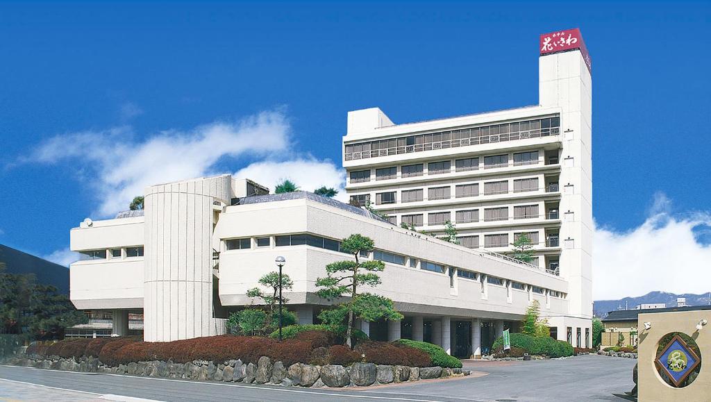 un grand bâtiment blanc avec un arbre devant dans l'établissement Hotel Hana Isawa, à Fuefuki