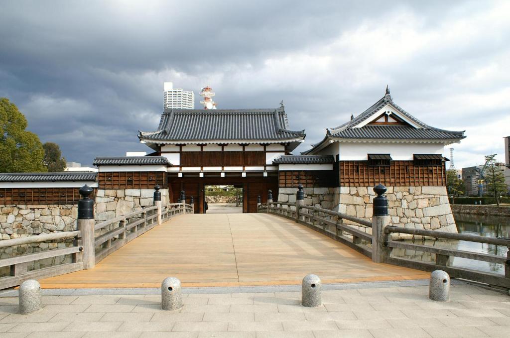 un bâtiment asiatique avec un pont sur une étendue d'eau dans l'établissement ホテルオリジン Hotel Origin 男塾ホテルグループ, à Hiroshima