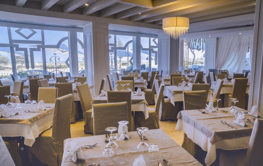 un restaurant avec des tables et des chaises blanches et des fenêtres dans l'établissement Hotel Principe, à Caorle