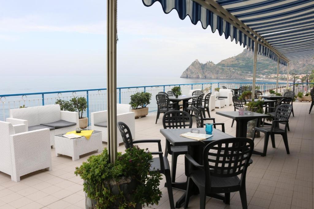 un patio avec tables et chaises et vue sur l'océan dans l'établissement Hotel Kennedy, à SantʼAlessio Siculo