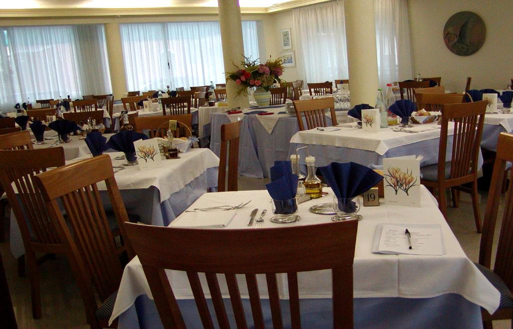 une salle à manger avec des tables et des chaises avec des nappes blanches dans l'établissement Pensione Villa Joli, à Lido di Jesolo