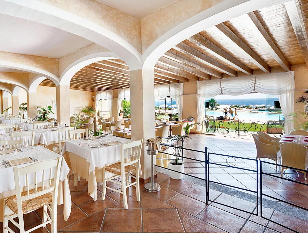 un restaurant avec des tables et des chaises blanches et un balcon dans l'établissement COLONNA RESORT, a Colonna Luxury Beach Hotel, Porto Cervo, à Porto Cervo