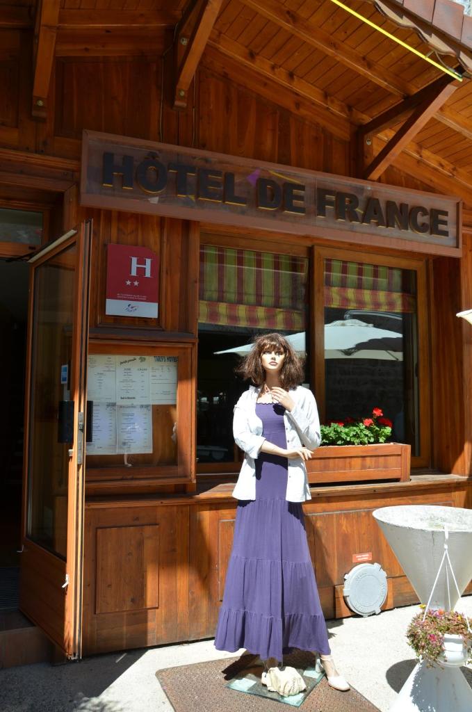 une femme debout devant une maison de franc dans l'établissement Hôtel de France, à Le Bessat