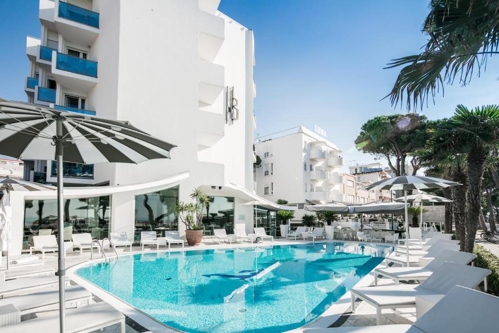 une piscine avec chaises et parasols à côté d'un bâtiment dans l'établissement Hotel Bellavista, à Lignano Sabbiadoro