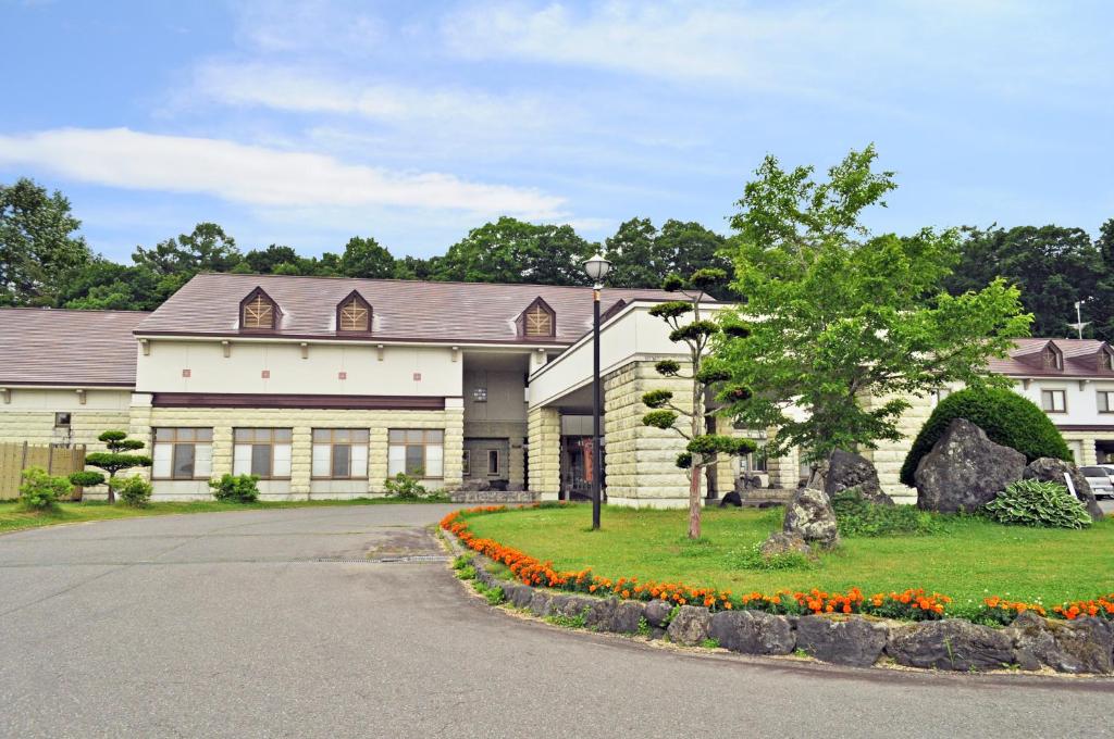 un grand bâtiment blanc avec un arbre et des fleurs dans l'établissement Kobushi no Yu Atsuma, à Atsuma