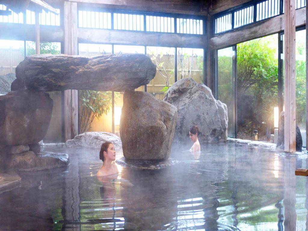 Deux femmes dans un bassin d'eau avec des rochers dans l'établissement Yuraku Hotel, à Awara