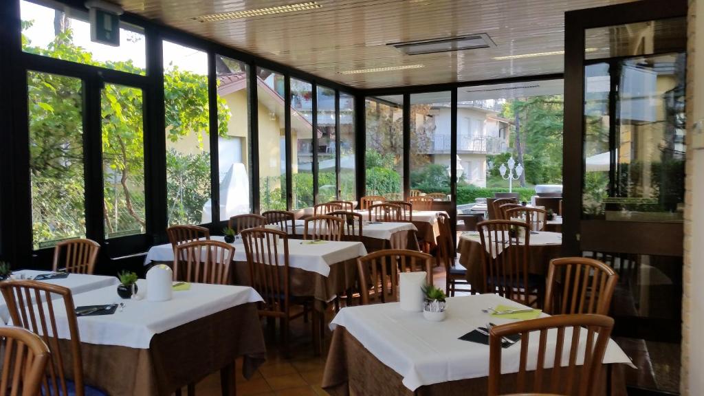 un restaurant avec des tables et des chaises blanches et des fenêtres dans l'établissement Hotel Acapulco, à Lignano Sabbiadoro