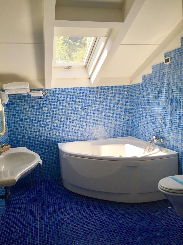 La salle de bains est pourvue de carrelage bleu, d'une baignoire et de toilettes. dans l'établissement Hotel Claila, à Francavilla al Mare