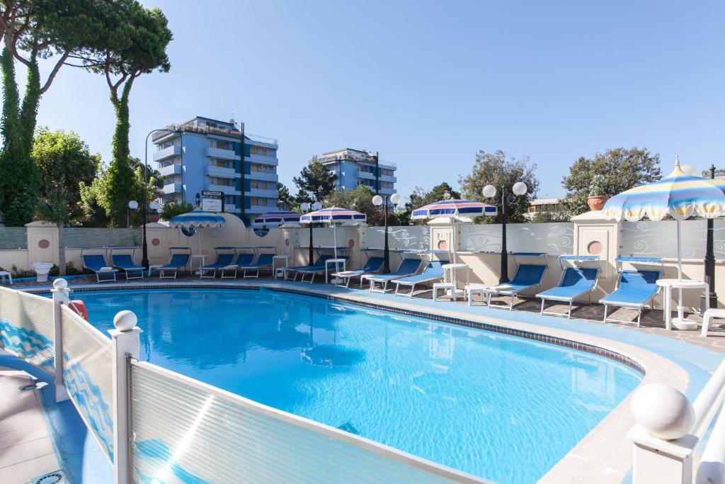 une grande piscine avec chaises longues et parasols dans l'établissement Hotel Levante, à Cervia