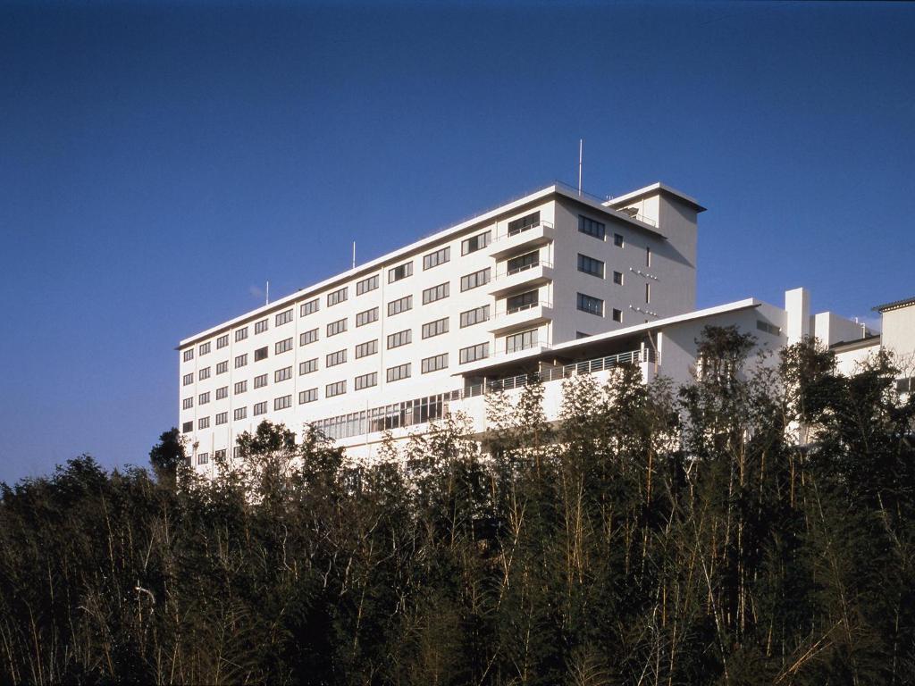 un bâtiment blanc avec des arbres devant dans l'établissement Nisshokan Shinkan Baishokaku, à Nagasaki