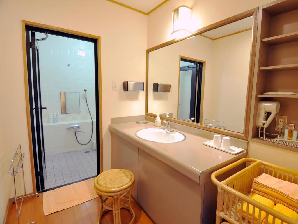une salle de bain avec un lavabo et une douche avec un miroir dans l'établissement Nisshokan Shinkan Baishokaku, à Nagasaki