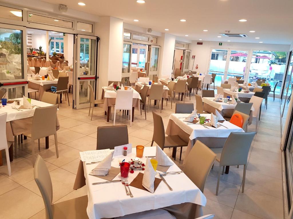 un restaurant avec des tables et des chaises blanches et des fenêtres dans l'établissement Hotel Helvetia, à Lignano Sabbiadoro