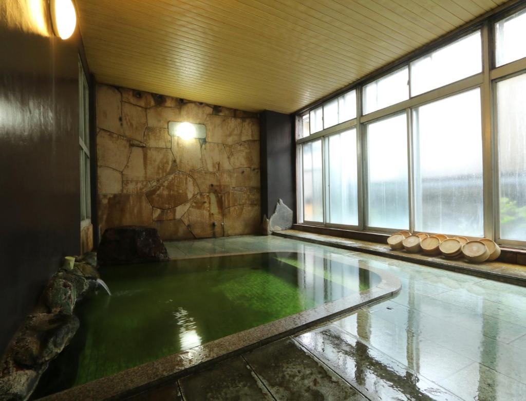 - une piscine d'eau verte dans une chambre avec fenêtres dans l'établissement Aritaya Ryokan, à Chikuma