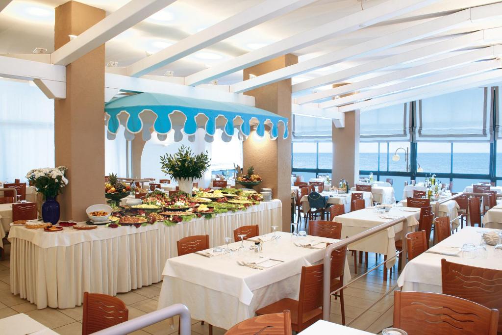 un restaurant avec des tables et des chaises blanches et l'océan dans l'établissement Hotel Manila, à Lido di Jesolo