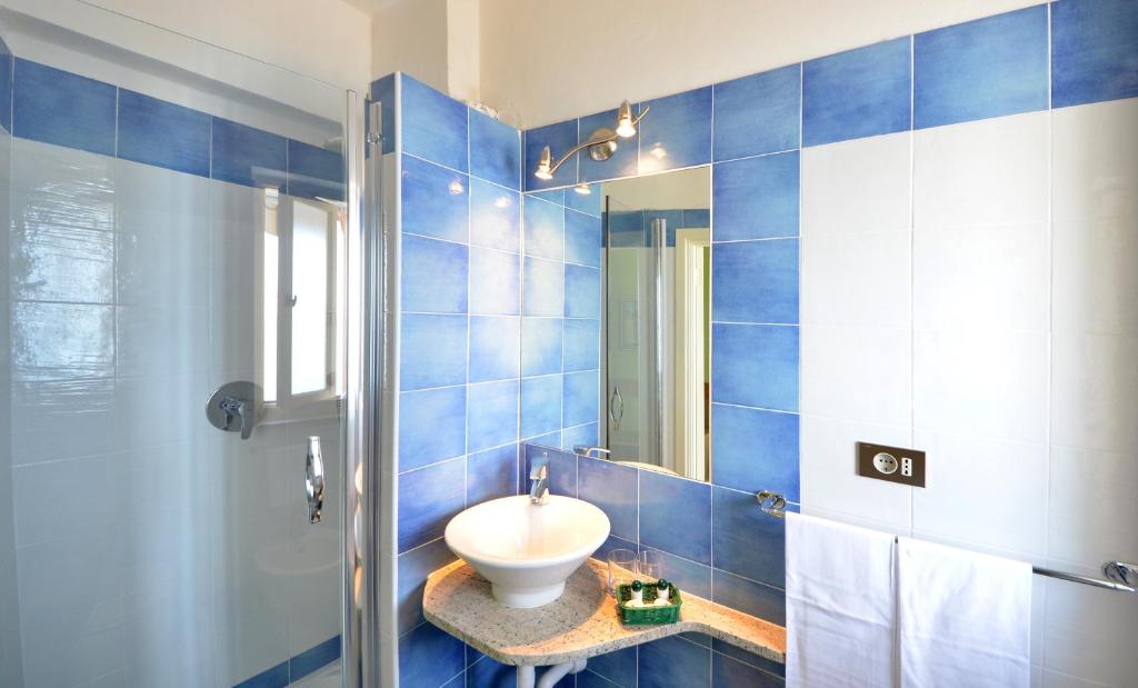 La salle de bains est pourvue de carrelage bleu, d'un lavabo et d'un miroir. dans l'établissement Hotel Stella Maris, à Capoliveri