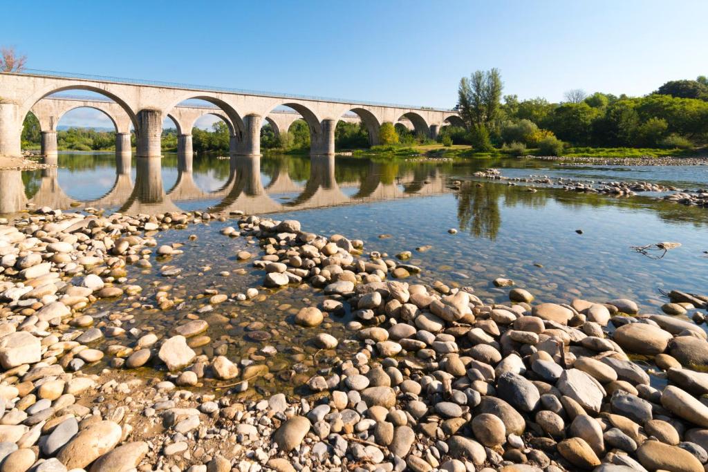 un pont sur une rivière avec des rochers dans l'eau dans l'établissement Camping RCN La Bastide en Ardèche, à Sampzon