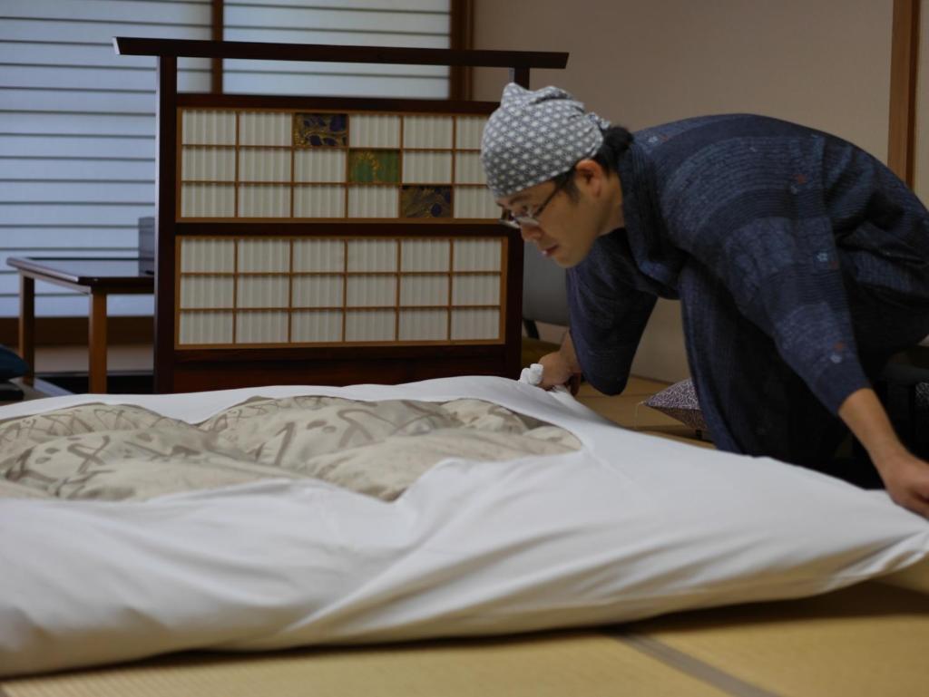 une femme penchée sur un lit avec une couverture dans l'établissement Nonohanatei komurasaki, à Shimoda