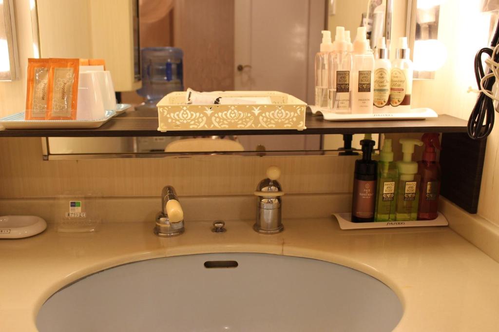 - un comptoir de salle de bains avec un lavabo et une étagère avec des bouteilles dans l'établissement Pal Annex Ogawa, à Kumamoto