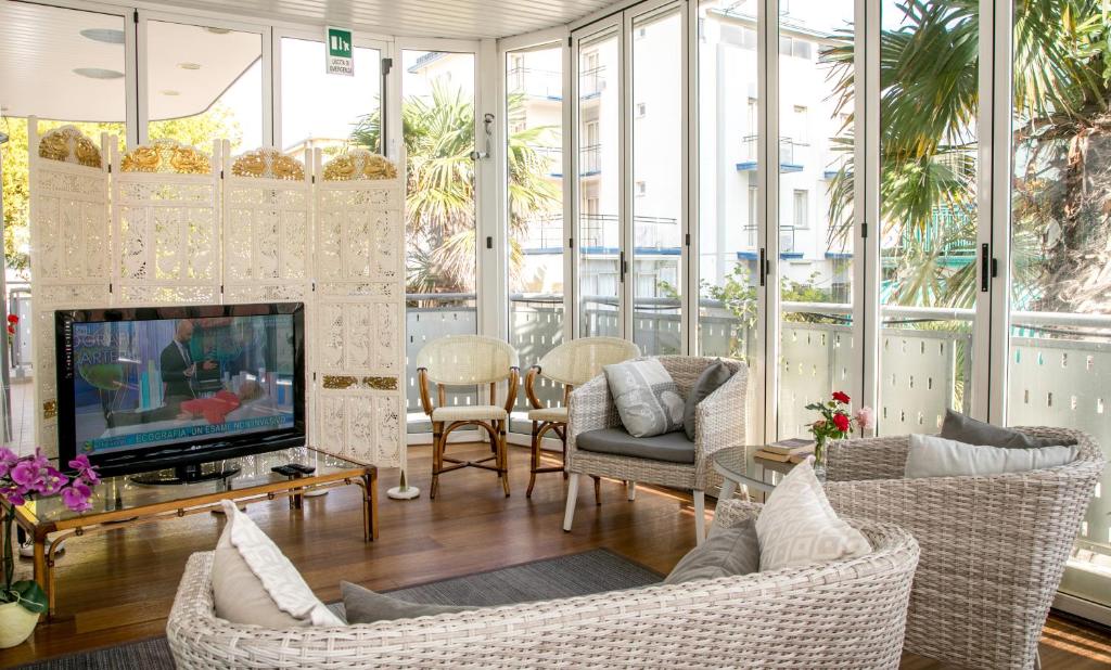 un salon avec une télévision, des chaises et des fenêtres dans l'établissement Hotel Helios, à Lido di Jesolo