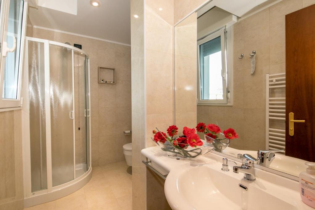 La salle de bains est pourvue d'un lavabo et d'une douche avec des fleurs rouges. dans l'établissement Hotel Helios, à Lido di Jesolo