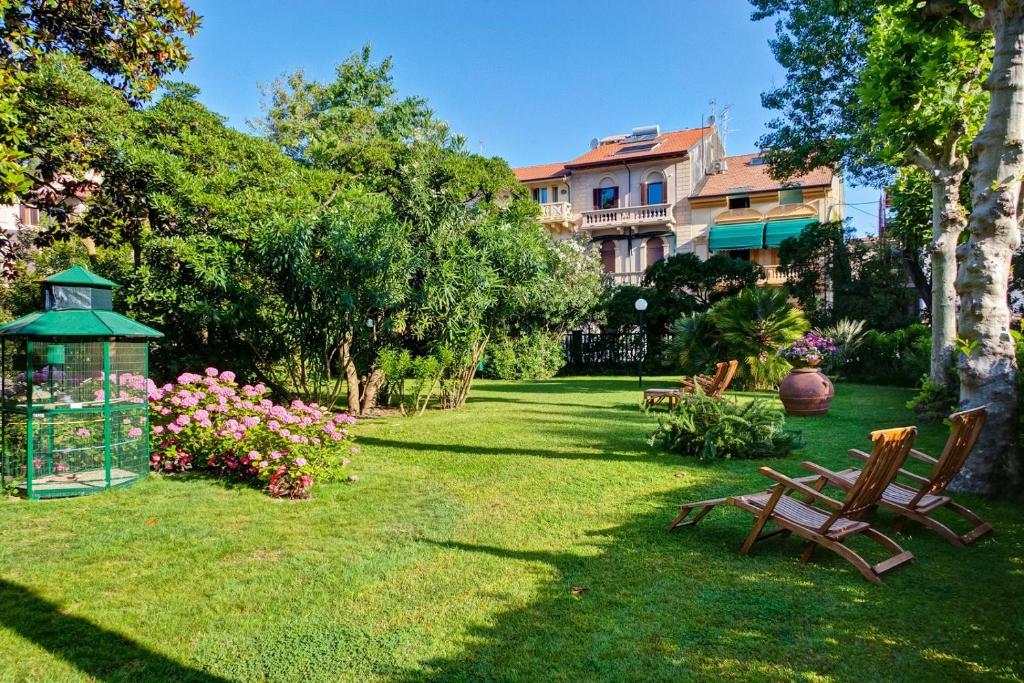 un jardin avec des chaises et des fleurs et un bâtiment dans l'établissement Grand Hotel Royal, à Viareggio