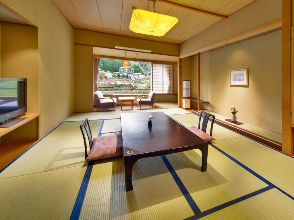 un salon avec une table, des chaises et une télévision dans l'établissement Hirugami Grand Hotel Tenshin, à Achi