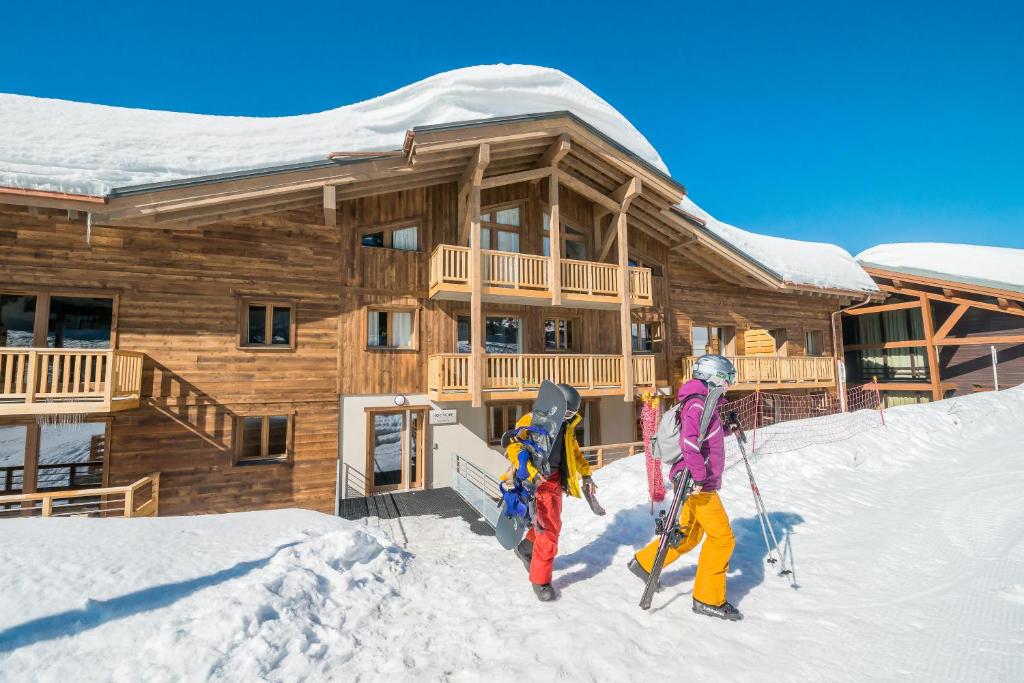 2 personnes debout dans la neige devant une cabane en rondins dans l'établissement Residence Le Roc Noir by Alpapart, à La Rosière
