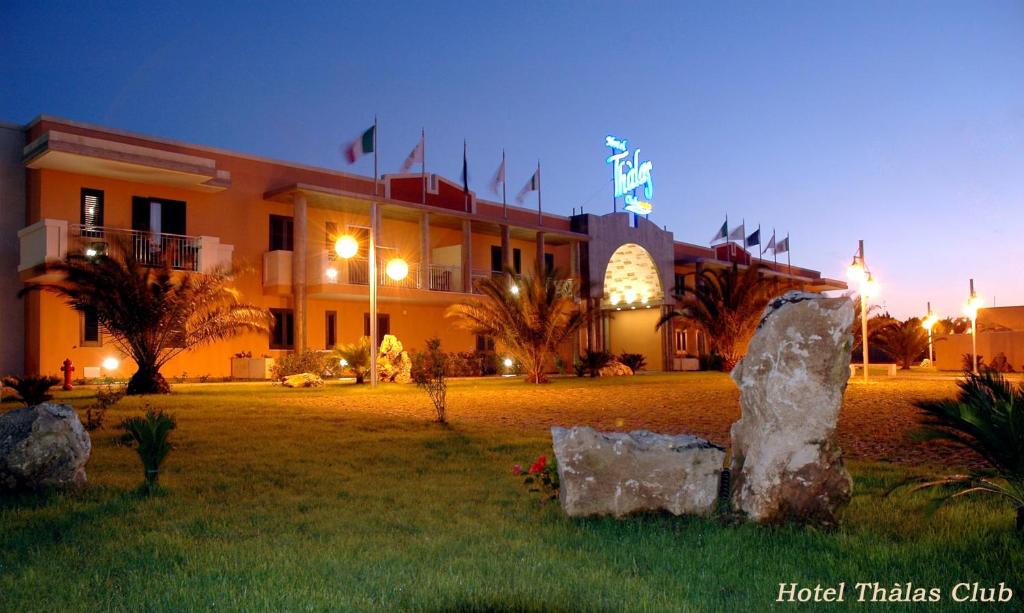 un grand bâtiment avec des drapeaux devant dans l'établissement Hotel Thàlas Club, à Torre dell'Orso
