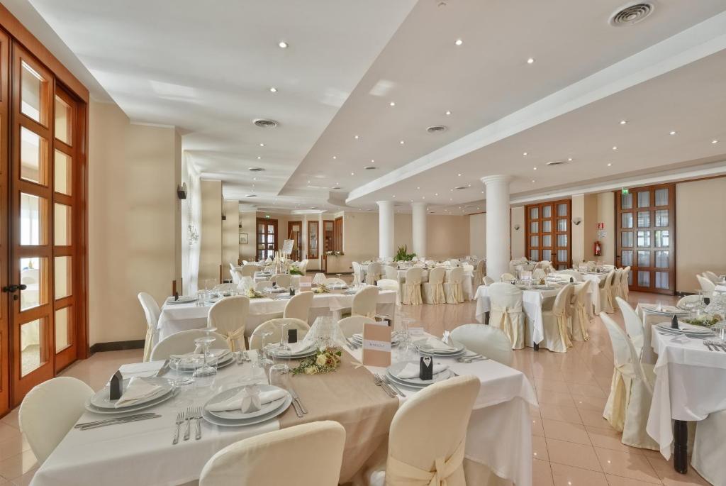 une grande salle de banquet avec des tables et des chaises blanches dans l'établissement Hotel Serenella, à Agropoli