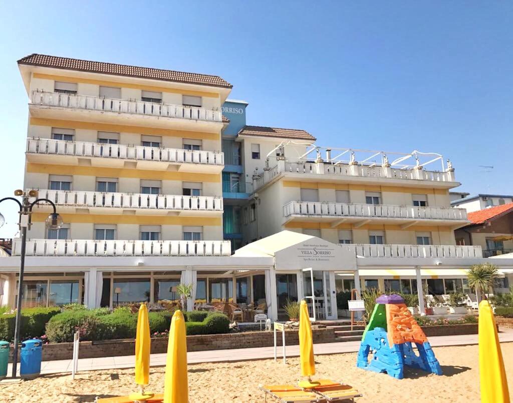 un hôtel avec des parasols jaunes et une aire de jeux sur le sable dans l'établissement Hotel Villa Sorriso, à Lido di Jesolo