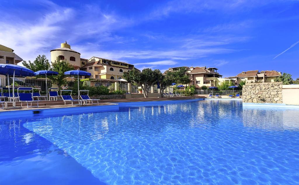 une grande piscine avec des chaises et des parasols bleus dans l'établissement Colonna Beach Hotel Marinella, à Marinella