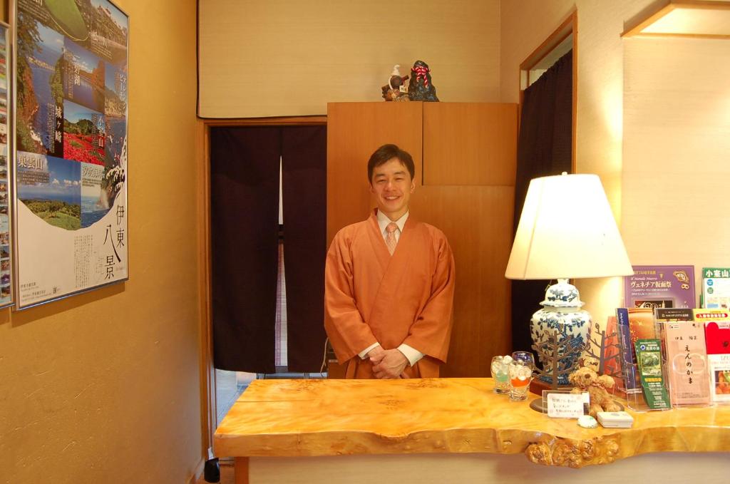 un homme debout à côté d'une table avec une lampe dans l'établissement Nasubi no Hana, à Itō