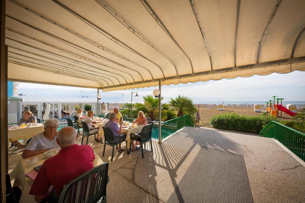 un groupe de personnes assises à des tables sous un parasol dans l'établissement Hotel Royal Garnì, à Caorle