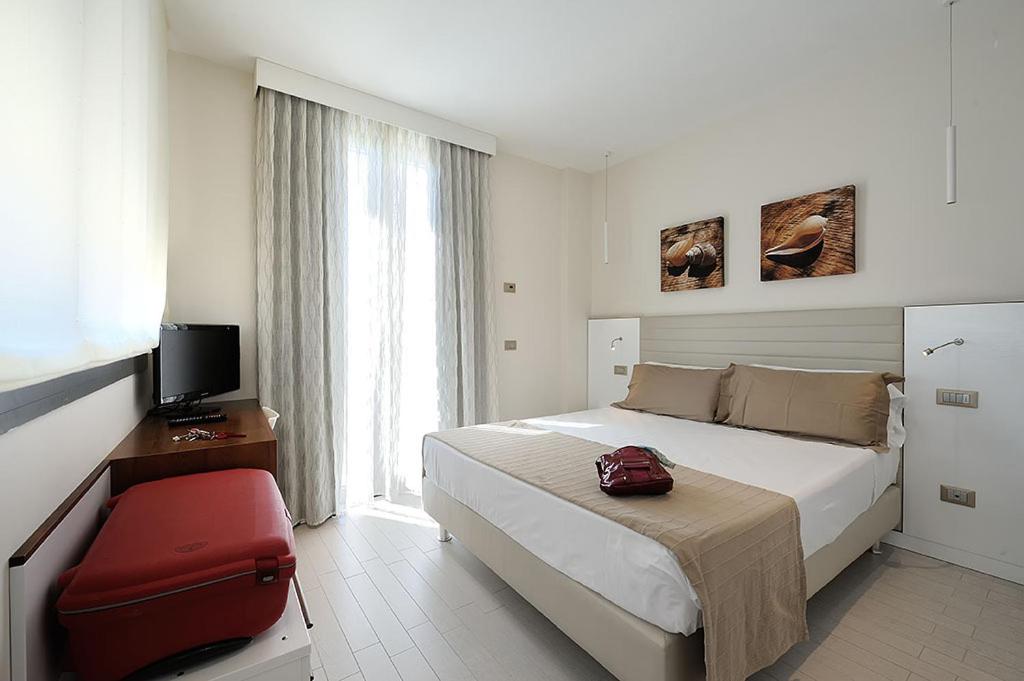 - une chambre avec un grand lit et une valise rouge dans l'établissement Hotel & Residence Cavalluccio Marino, à Rimini