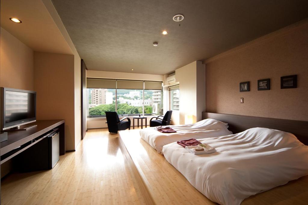 une chambre d'hôtel avec deux lits et une télévision à écran plat dans l'établissement Ito Yukitei, à Itō