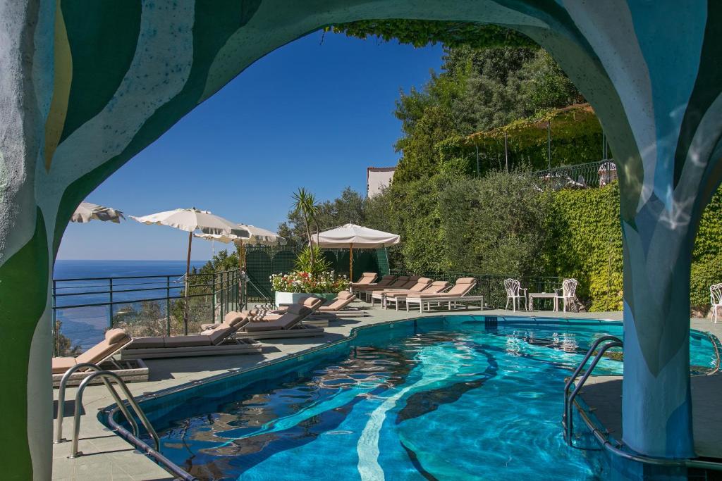 une piscine avec des chaises et l'océan en arrière-plan dans l'établissement Hotel Le Agavi, à Positano