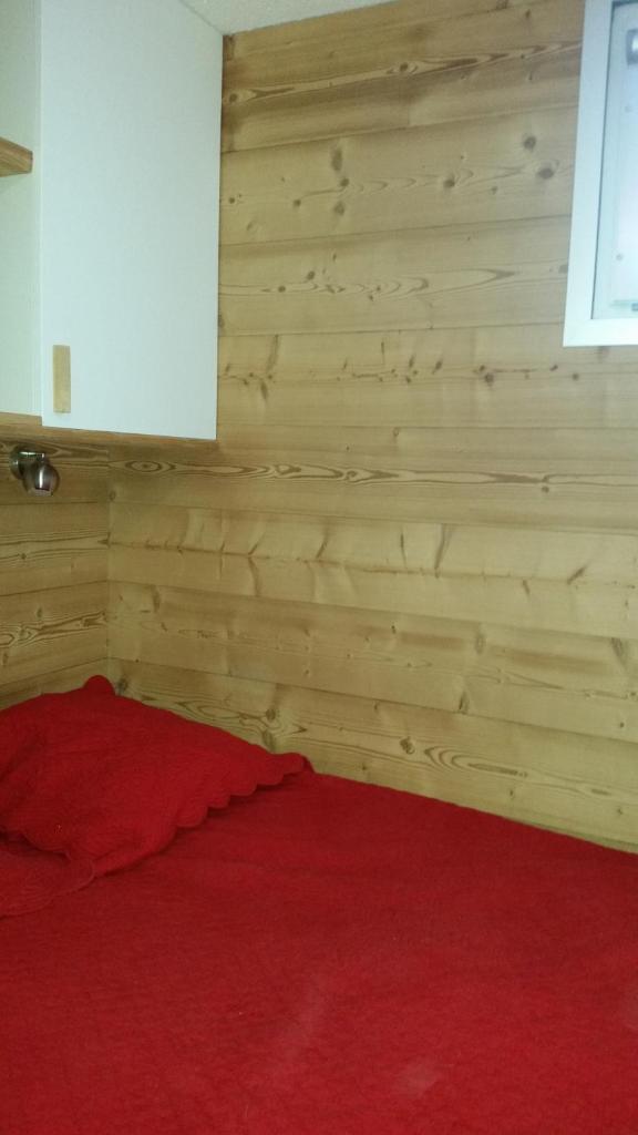 Cette chambre comprend un lit rouge et un mur en bois. dans l'établissement Studio COTE BRUNE 2 ALPES, à Les Deux Alpes