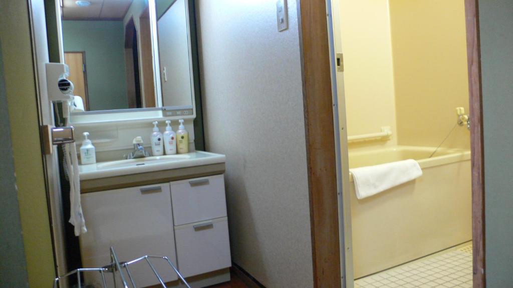 une salle de bain avec un lavabo, un miroir et une baignoire dans l'établissement Yuttarino-Sato Inaka, à Achi