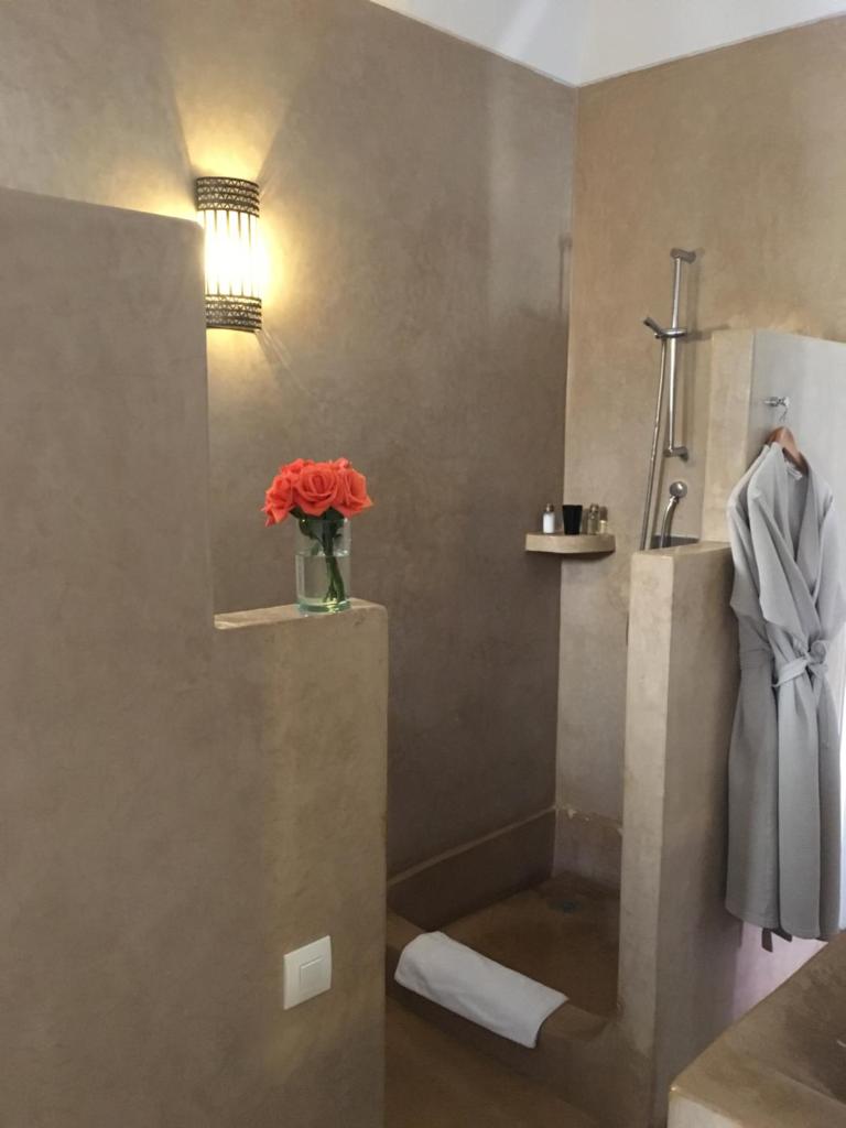 La salle de bains est pourvue d'une douche et d'un vase de fleurs rouges. dans l'établissement Riad Dar More, à Marrakech