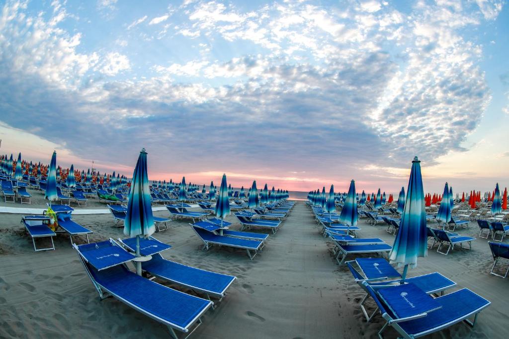 - un groupe de chaises de plage bleues et de parasols sur une plage dans l'établissement Hotel Riziana, à Cervia