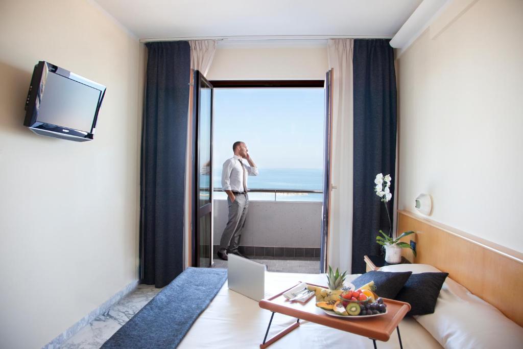 un homme debout dans une chambre d'hôtel regardant par la fenêtre dans l'établissement Hotel Mistral, à Termoli